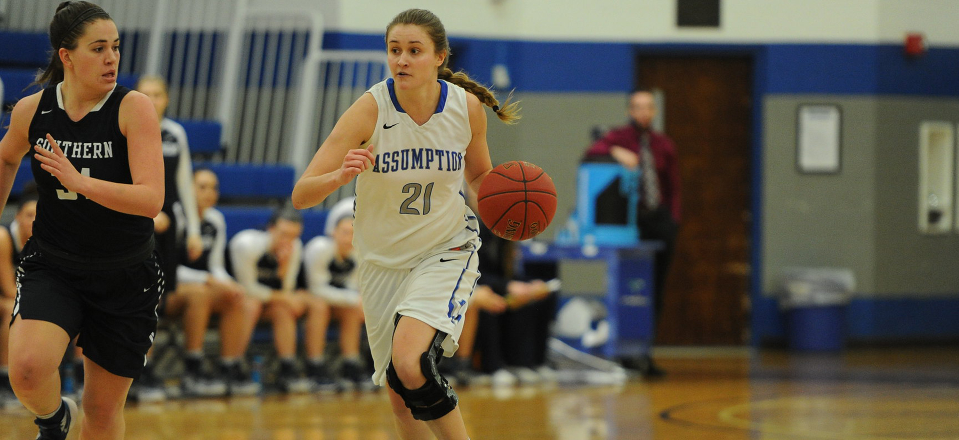 A member of the Assumption Women's Basketball team dribbles a ball up the court.