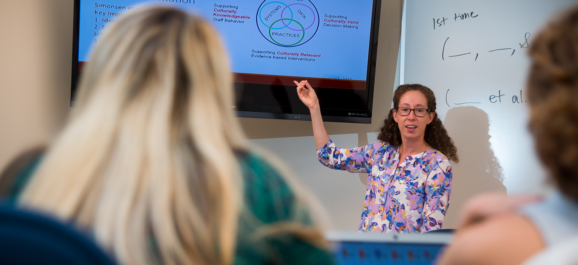 An Assumption University professor teaching in a classroom on the Worcester, Massachusetts campus with a television monitor.