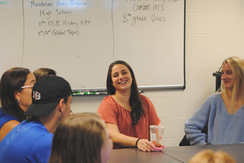 Students gathered around a circle table with a whiteboard in the background.