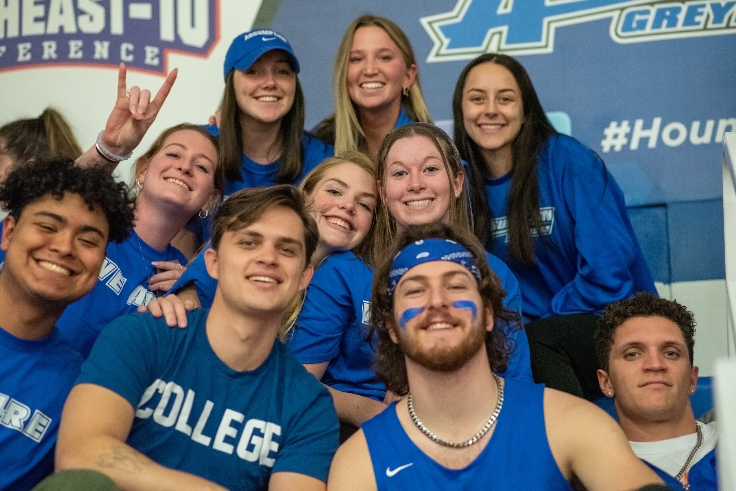 Group of students sitting together smiling wearing their blue Assumption pride shirts