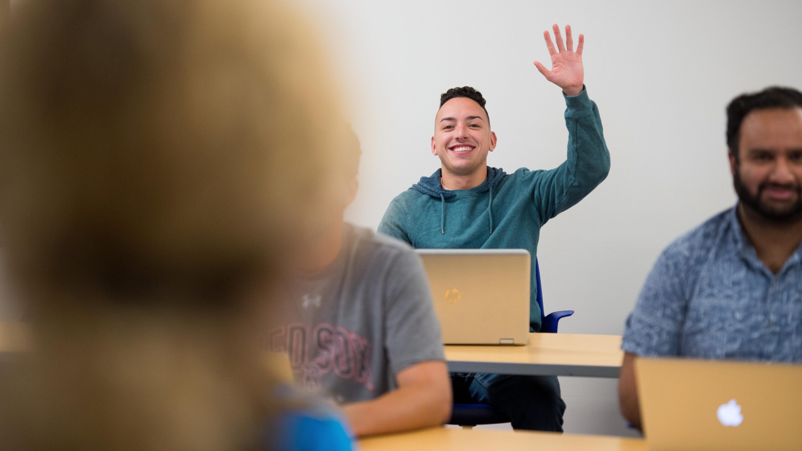 Male student in a blue sweatshirt raising his hand in a classom