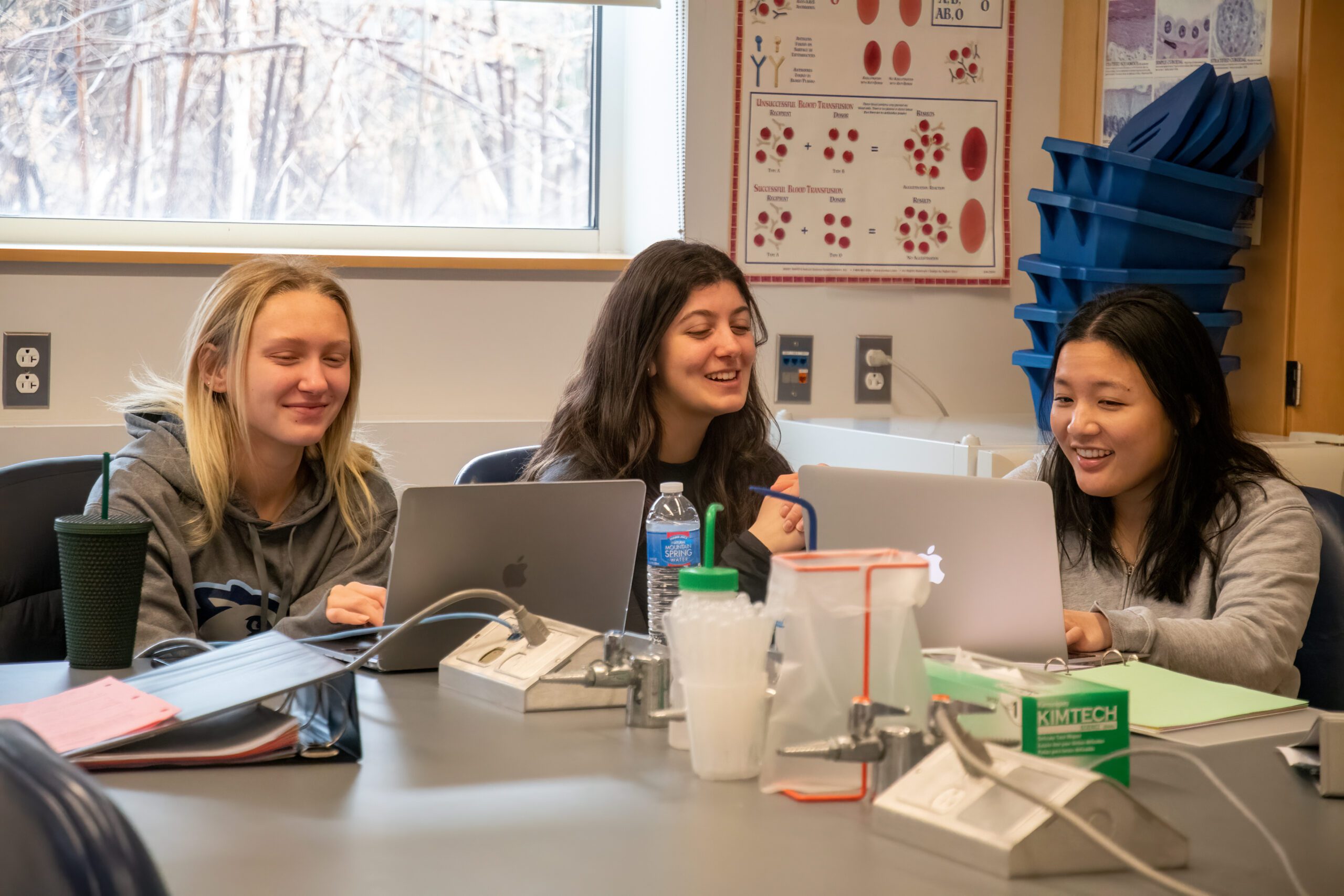 Three female students sitting around a table working together with their laptops open