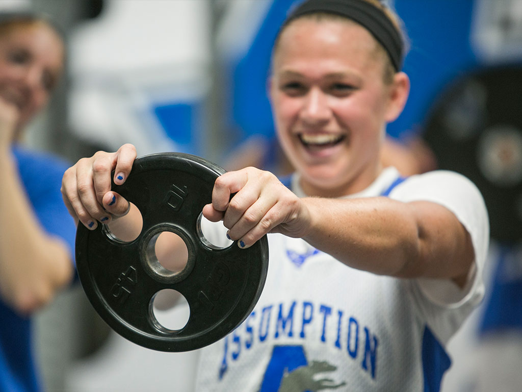 Assumption student holding a weight during a workout